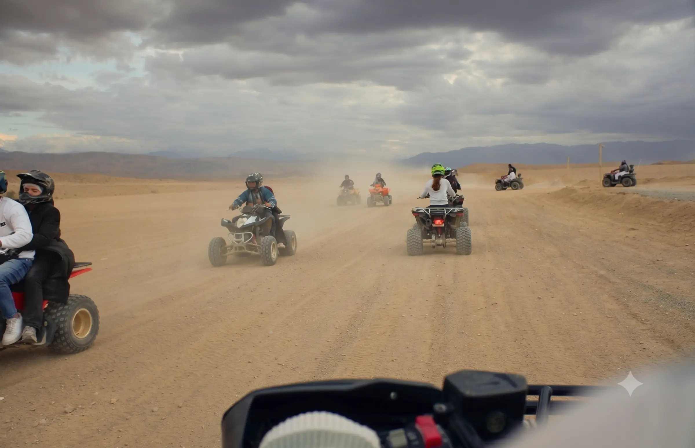 Quad bikes raising dust on a desert track under a stormy sky.