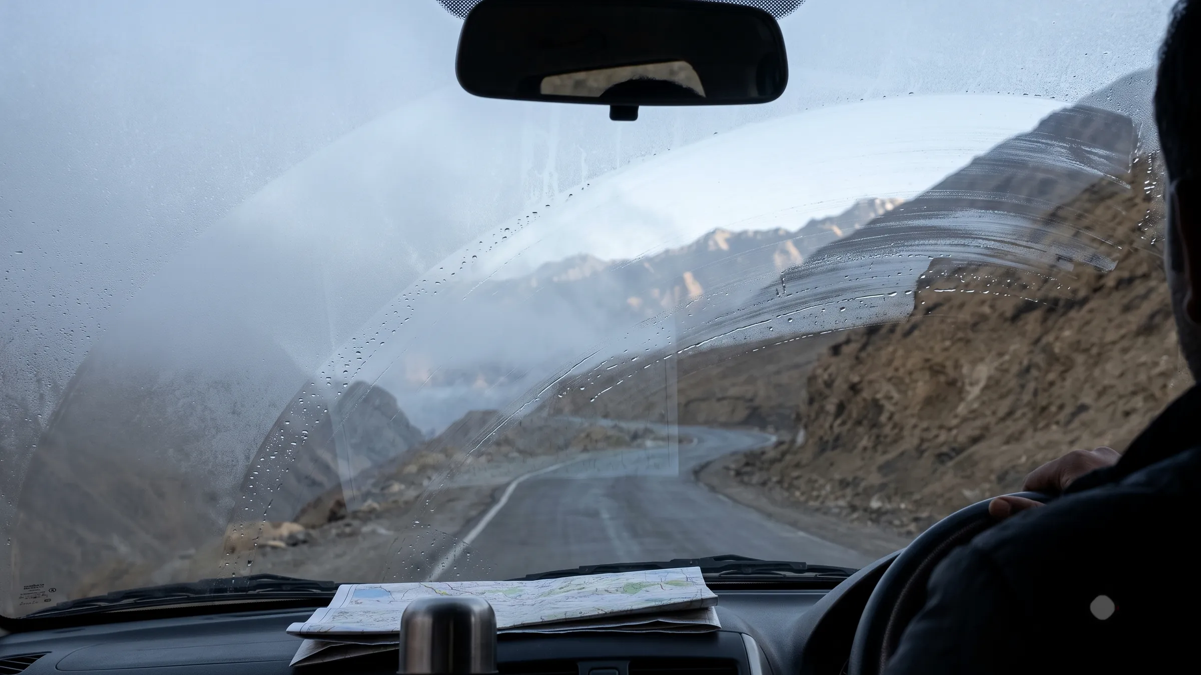 Looking through the windscreen at a mountain road, a map open on the dashboard.